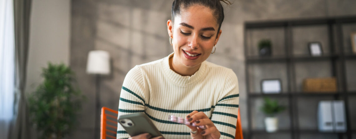 Woman smiling while looking at phone, representing positive attitudes toward mental health medication myths and treatment