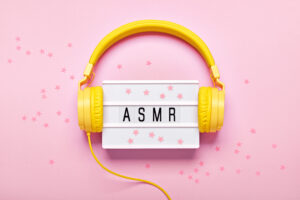 Yellow headphones, ASMR letters lightbox and confetti on pink background. ASMR Stress-relieving sounds concept, flat lay.
