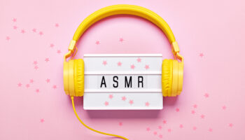 Yellow headphones, ASMR letters lightbox and confetti on pink background. ASMR Stress-relieving sounds concept, flat lay.
