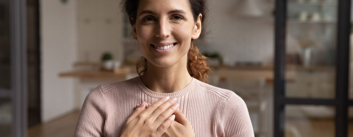 Head shot portrait smiling woman folded hands on chest, feeling self-compassion