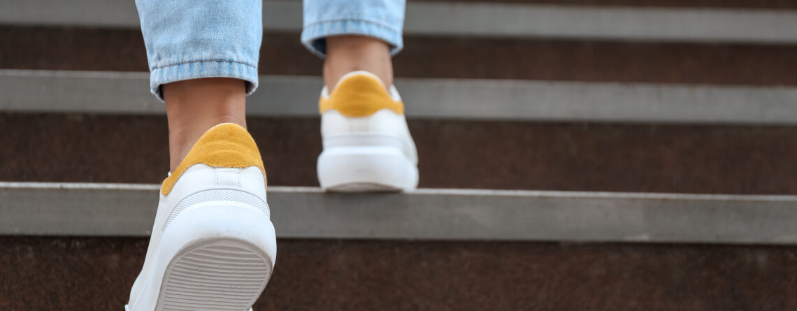 Close-up of a person wearing white and yellow sneakers, walking up concrete stairs, symbolizing the journey of recovery.