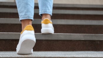 Close-up of a person wearing white and yellow sneakers, walking up concrete stairs, symbolizing the journey of recovery.