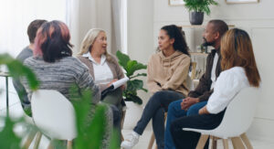 Diverse group of people sitting in circle during group therapy session with therapist