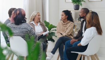 Diverse group of people sitting in circle during group therapy session with therapist