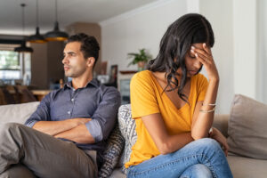 Young couple sitting on couch after an argument. Sad woman sitting with hand on head after quarrel with boyfriend at home. Angry couple ignoring each other on the sofa, having relationship troubles.