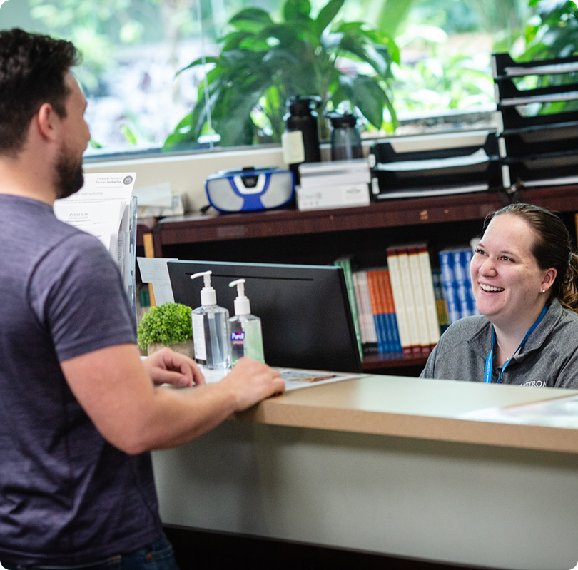 Smiling man speaking to a woman behind a counter in a friendly conversation.