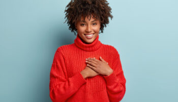 Photo of emotional dark skinned female touches heart with both palms, demonstrates thankful gesture, has good natured expression, expresses great sympathy, gratitude with honesty, feels love