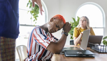 An African-American woman sitting in a conference room experiencing workplace anxiety